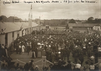 Photographie noir et blanc montrant une foule de dos, rassemblée devant une tribune d'hommes en train de discourir.