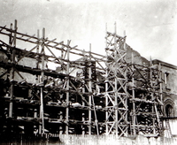 Photographie noir et blanc montrant un échafaudage devant un bâtiment en construction.