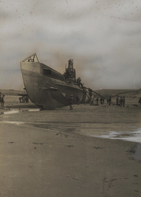 Photographie noir et blanc montrant un grand sous-marin échoué sur une plage.