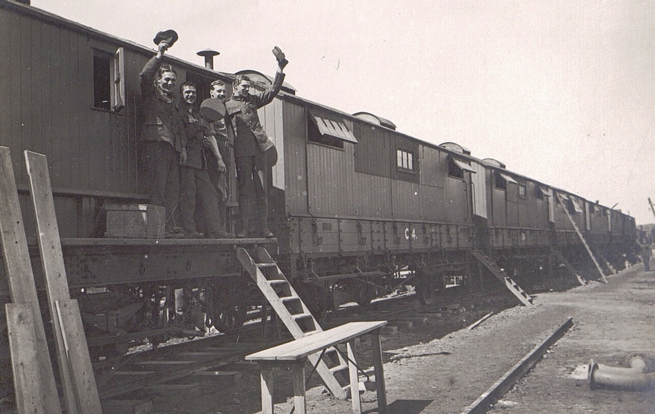 Photographie noir et blanc montrant quatre militaires riant et levant leur chapeau, devant la porte d'un wagon.