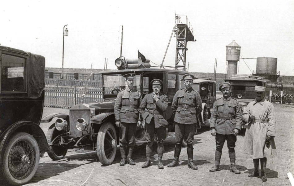 Photographie noir et blanc montrant cinq militaires posant devant des voitures.
