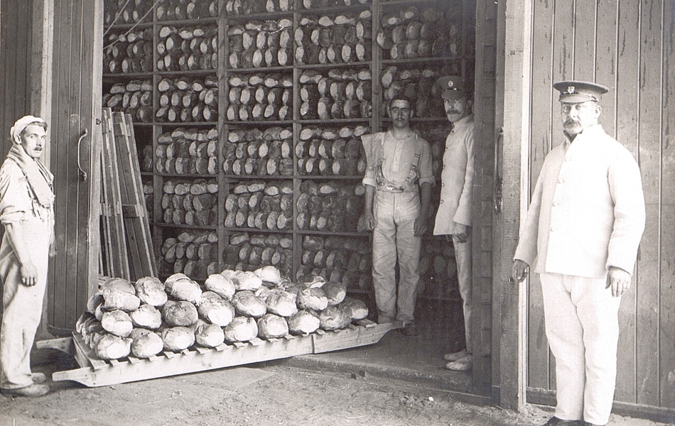 Photographie noir et blanc montrant quatre hommes en tenue de boulanger, posant devant un entrepôt de pain.