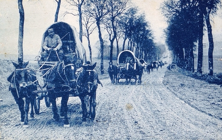 Carte postale monochrome montrant des charrettes conduites par des soldats se suivant sur une route de terre.