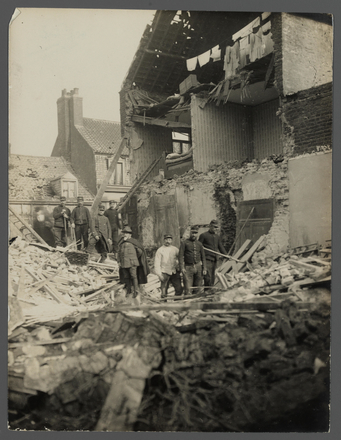 Photographie noir et blanc montrant une maison éventrée par un bombardement devant laquelle pose un groupe d'hommes.