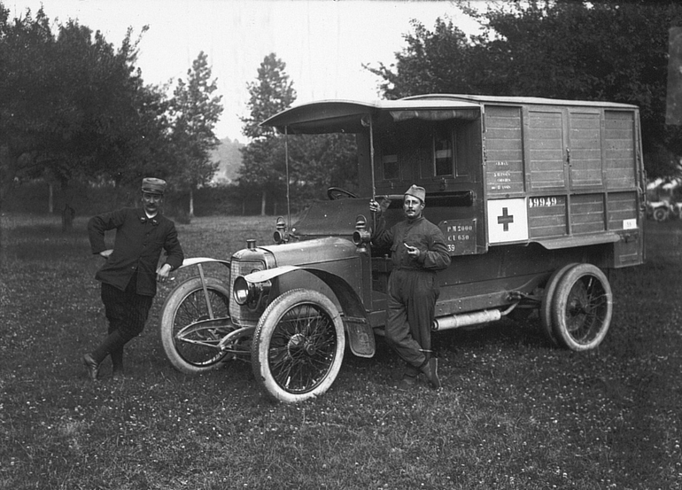Photographie noir et blanc montrant une ambulance militaire devant laquelle posent deux hommes.
