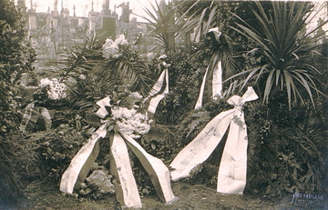 Photographie noir et blanc montrant des gerbes et des couronnes de fleurs dans un cimetière.