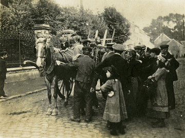 Photographie noir et blanc montrant des hommes, des femmes et des enfants regroupés autour d'une charrette chargée de nombreux meubles et bagages.