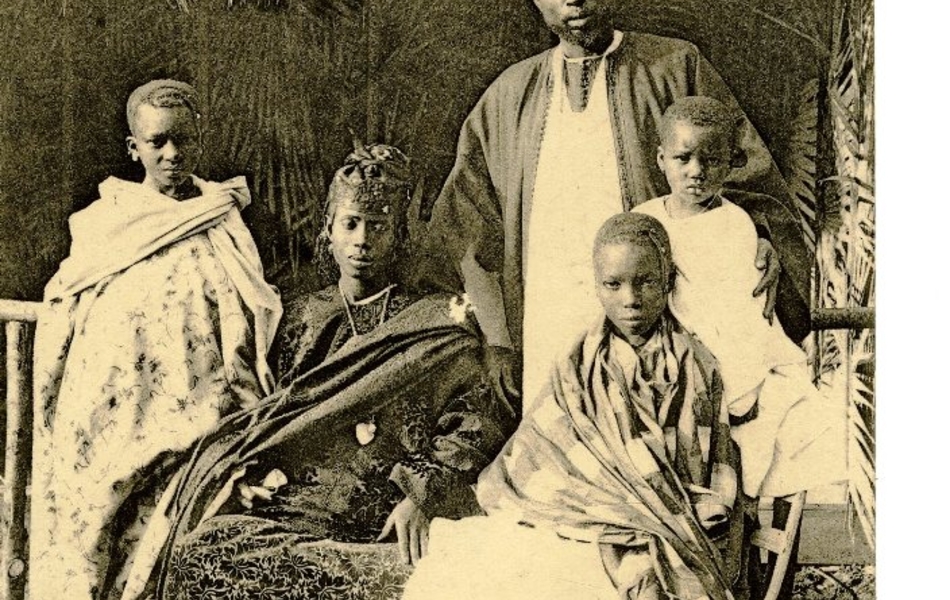 Carte postale noir et blanc d'une famille africaine posant devant une case. Les trois enfants entourent leurs parents.