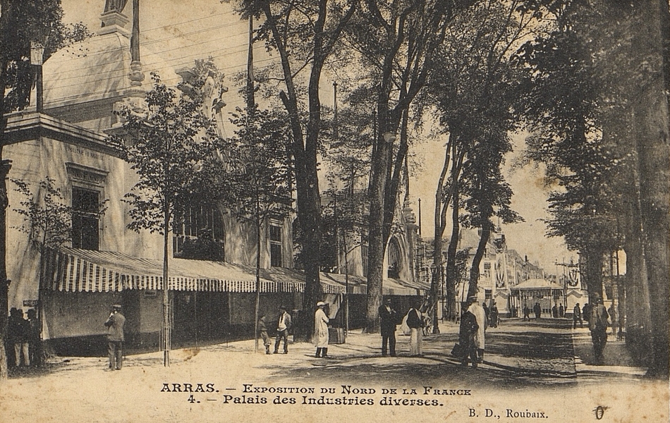 Carte postale noir et blanc montrant une allée bordée d'arbres et d'un grand bâtiment. Tout au bout, on aperçoit des grilles et au-delà des toits de maisons. Des promeneurs marchent à l'ombre des arbres.