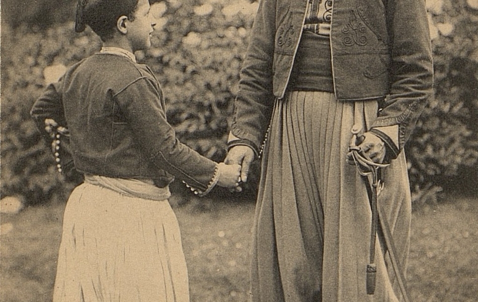 Carte postale noir et blanc montrant un jeune garçon de trois-quart serrant la main à un homme tourné vers l'objectif. Tous deux se sourient et portent des habits orientaux (culotte large et turban).