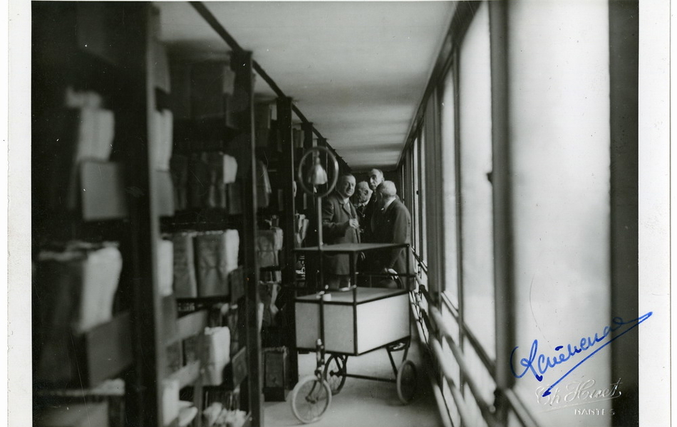 Photographie noir et blanc montrant quatre hommes dans une travée d'un magasin d'archives.