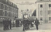 Carte postale noire et blanc montrant des soldats au garde à vous dans la cour d'une caserne.