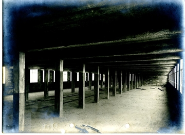 Photographie noir et blanc d'une vaste salle en travaux, dont le plafond est soutenu par des colonnes en béton.