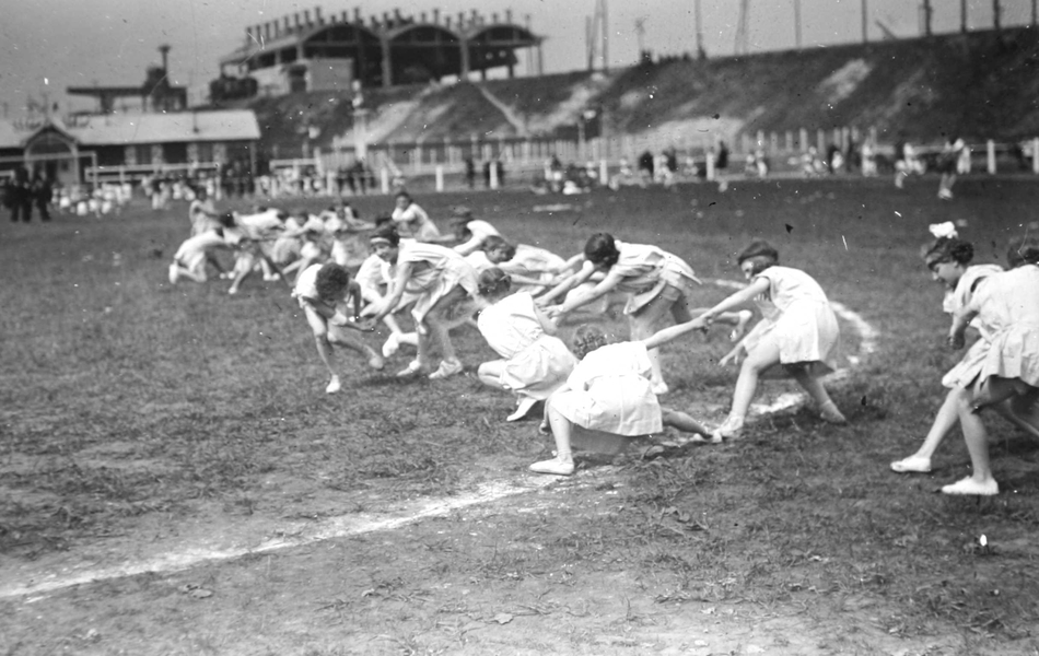Photographie noir et blanc montrant des jeunes filles faisant de la gymnastique sur un stade.