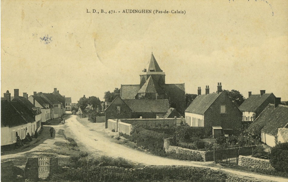 Carte postale en noir et blanc représentant l’église et le village d’Audinghen, composé de petites maisons bordées de jardins, séparées par un chemin en terre battue
