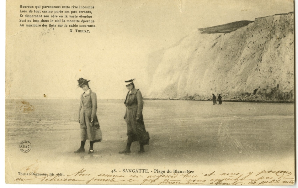 Carte postale en noir et blanc de la plage et des falaises derrière. Deux femmes chapeautées avancent sur le sable