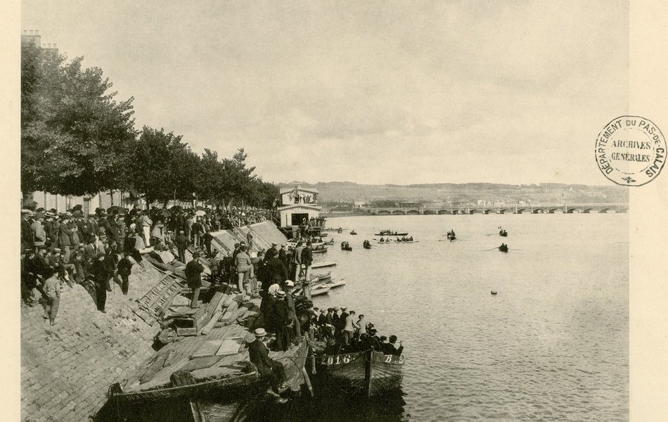 Photographie noir et blanc du rivage d'un fleuve, au bord duquel s'amasse une foule. Au second plan, sur le fleuve, se trouvent quelques avirons.