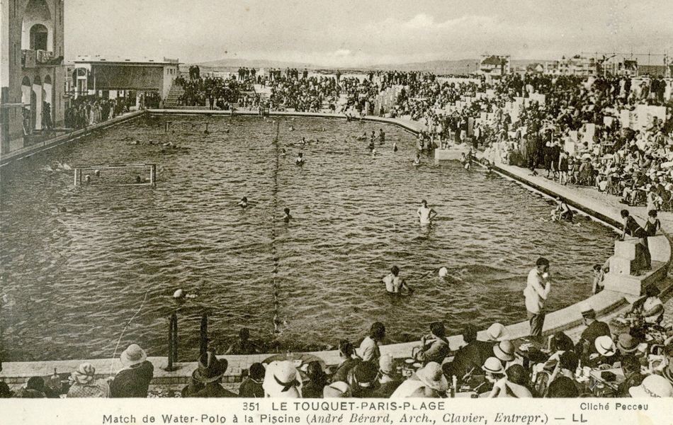 Photographie noir et blanc d'une piscine extérieure art-déco très fréquentée.