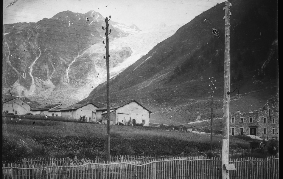 Photographie noir et blanc montrant de petites maisons au pied de montagnes.