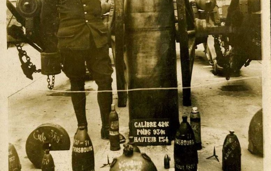 Photographie représentant un militaire dans la cour d'un hôtel particulier, entouré d'obus, de pièces d'artillerie et de matériel de la guerre de 1870.
