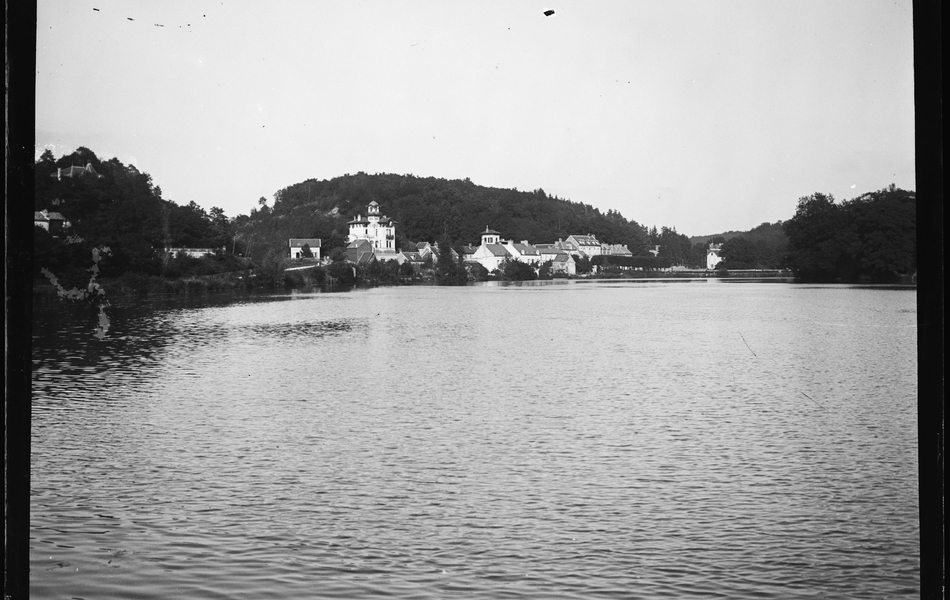 Photographie noir et blanc montrant un lac. À l'arrière plan, sur le rivage, on voit un groupe de bâtiments.