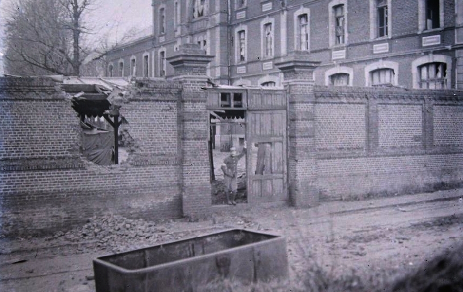 Photographie représentant un militaire se tenant debout, au portail d'un bâtiment. 