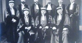 Photographie noir et blanc de neuf juges en habit posant sur deux rangées pour le photographe.