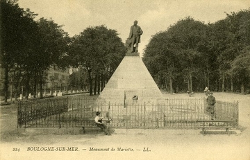 Carte postale en noir et blanc représentant une pyramide sur laquelle est posée une statue d'Auguste Mariette. Entouré de grillages et de bancs publics, ce monument se trouve dans un parc.