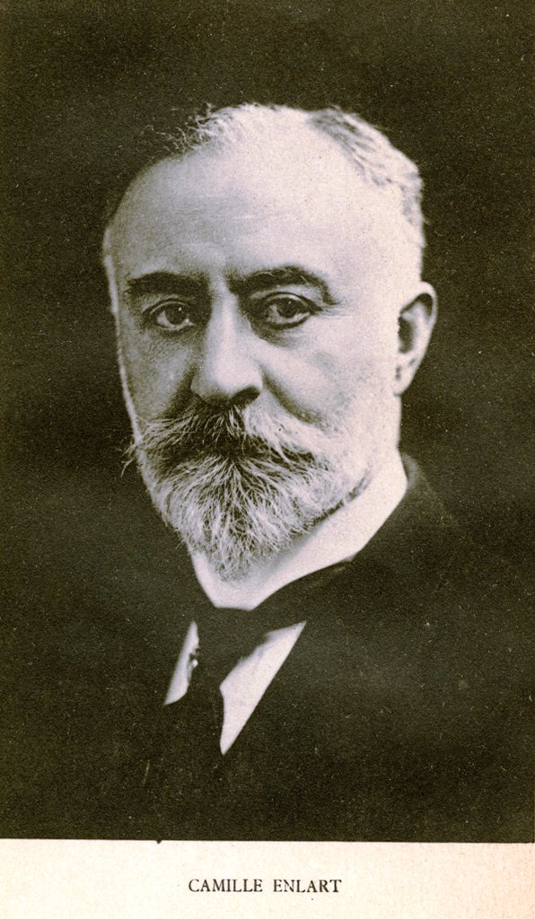 Photographie noir et blanc de Camille Enlart de trois-quart, portant une moustache et une barbe blanche, ainsi qu'un costume et une cravate sombres. 