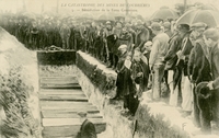 Carte postale noir et blanc montrant une foule rassemblée autour d'une fosse. Au premier rang, un prêtre.