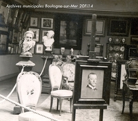 Photographie noir et blanc montrant une salle de musée comprenant mobilier, statues et tableaux.