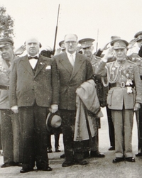 Photographie noir et blanc montrant des hommes debout, dont certains sont en costume militaire et au garde-à-vous.