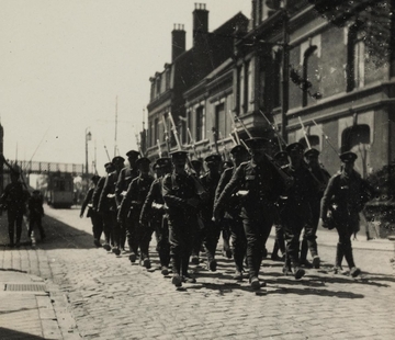 Photographie noir et blanc montrant un défilé de soldats dans une rue pavée.