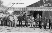 Carte postale noir et blanc montrant un groupe d'hommes posant de vant un avion et un hangar.