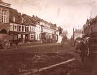 Photographie sepia montrant une rue bordée de maison. Au milieu, une statue sur un piédestal.