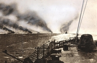 Photographie noir et blanc prise depuis un bateau en mer et qui montre d'autres navires au large, d'où s'échappent de la fumée.