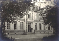 Photographie noir et blanc montrant un château dans un parc arboré. Sur le perron, on distingue la silhouette d'un homme.