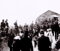 Photographie noir et blanc montrant un groupe de soldats défiler devant des civils.