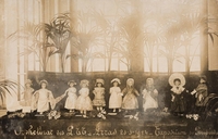 Photographie sépia montrant des poupées alignées devant une tenture.