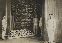 Photographie noir et blanc montrant trois hommes posant aux côtés d'une armoire remplie de miches de pain.