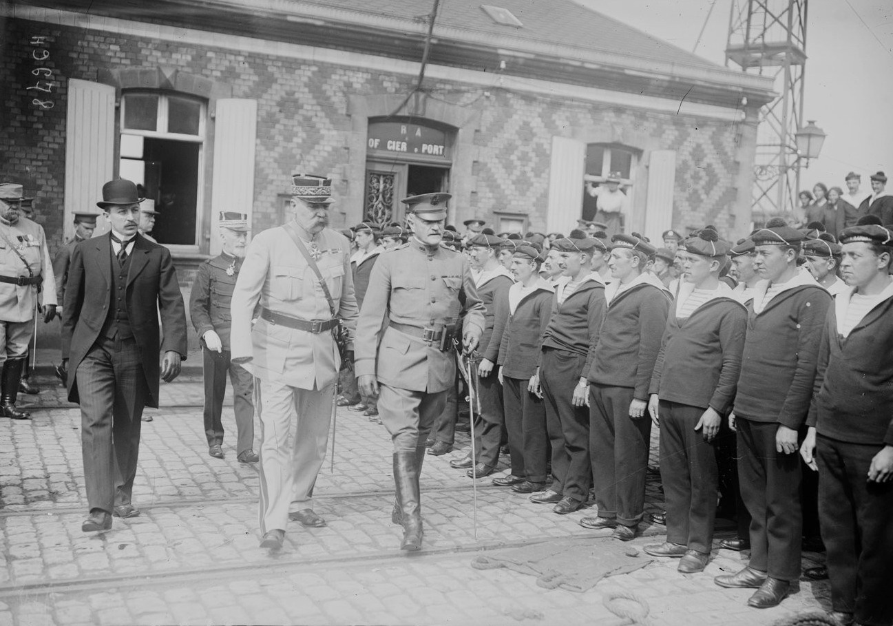 Photographie noir et blanc montrant une délégation d'hommes habillés en tenue militaire en train de passer devant des soldats au garde-à-vous.