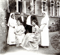 Photographie noir et blanc montrant un soldat au bras bandé posant aux côtés d'infirmières et d'un homme en habit.