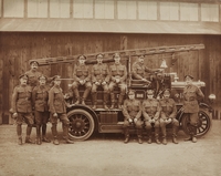 Photographie sépia montrant un groupe de pompiers devant un de leurs véhicules.