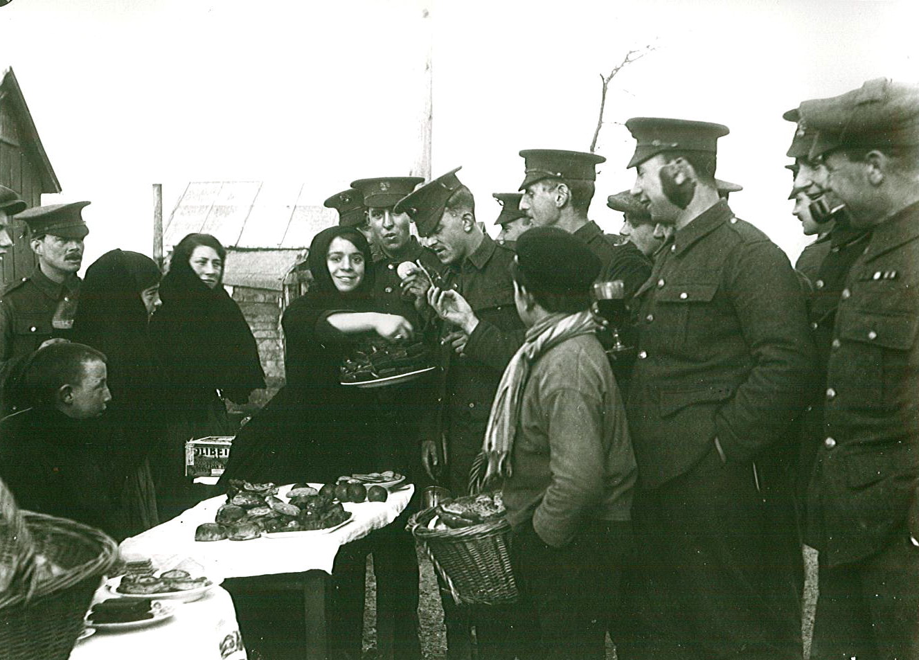 Photographie noir et blanc montrant des soldats regroupés autour de l'échoppe de deux femmes et d'enfants.