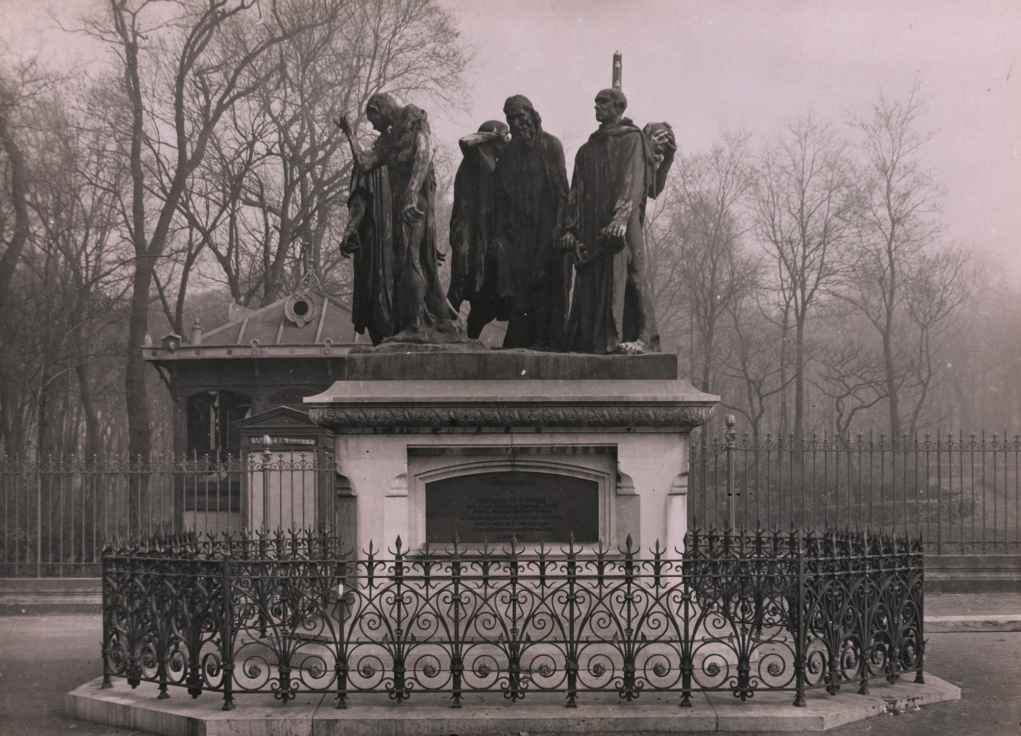 Photographie noir et blanc montrant un groupe de personnages en bronze sur un piédestal.