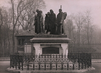 Photographie noir et blanc montrant un groupe de personnages en bronze sur un piédestal.
