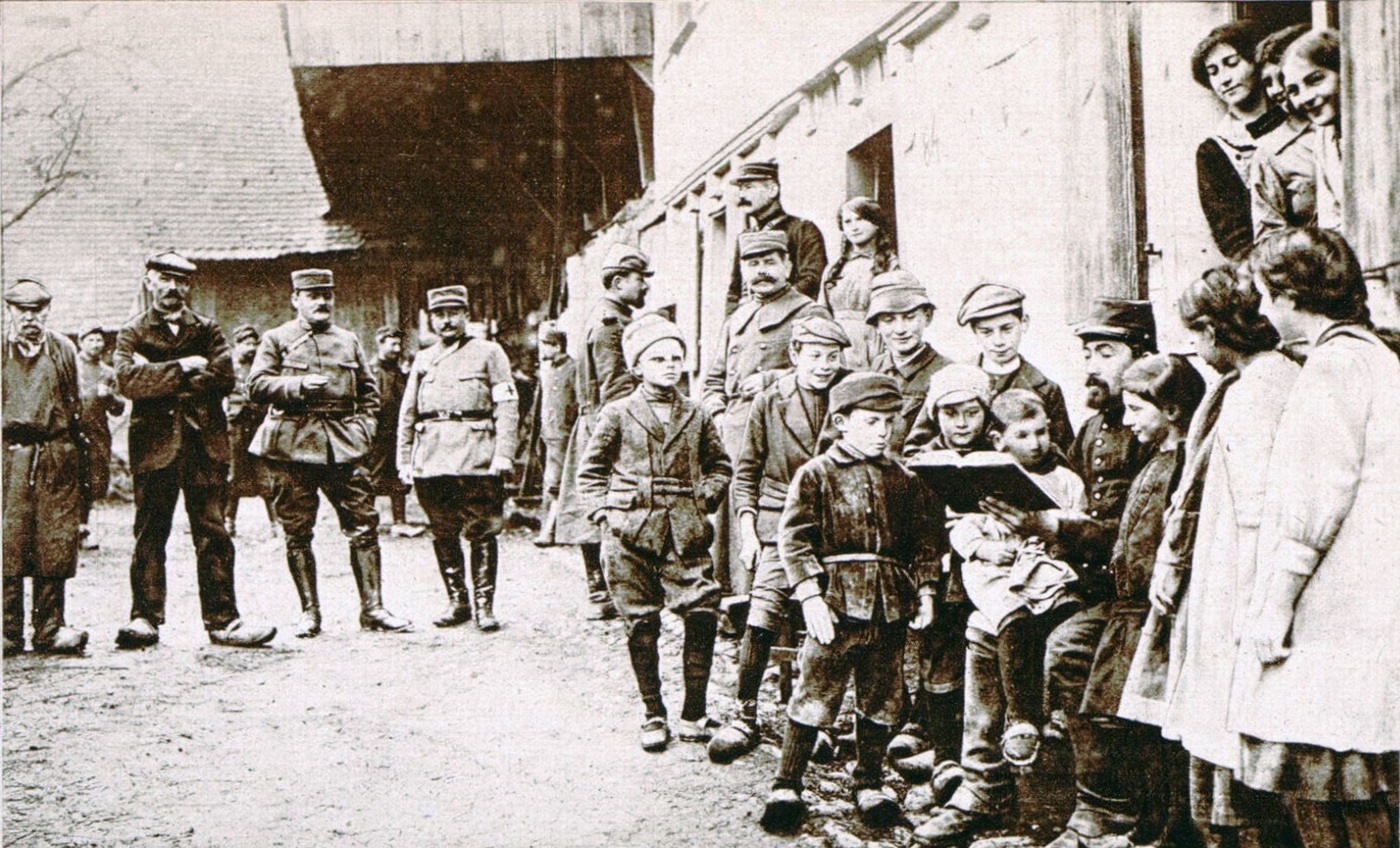 Photographie noir et blanc montrant des enfants regroupés autour d'un soldat faisant la lecture dans une cour.