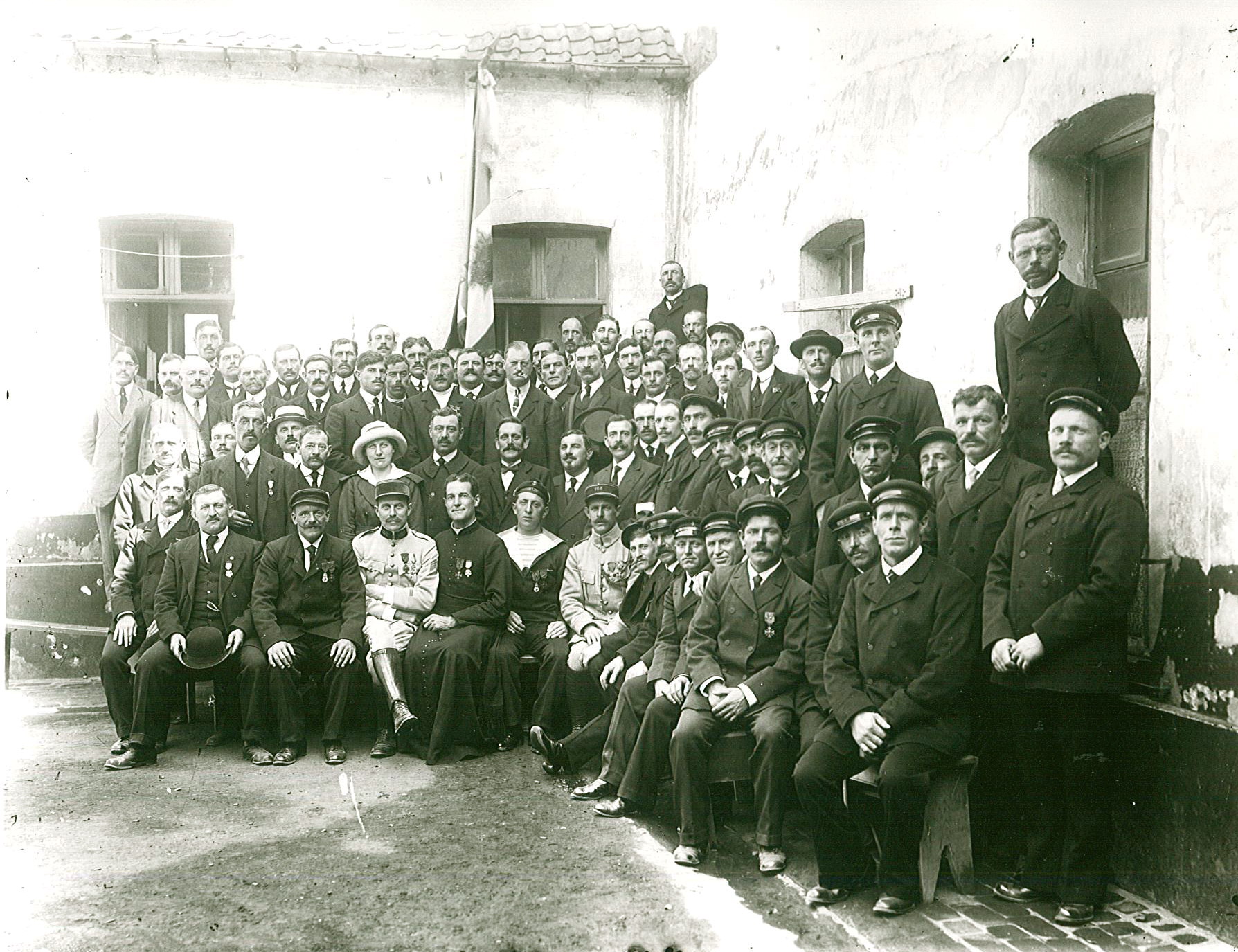 Photographie noir et blanc montrant un groupe d'hommes réunis. Certains portent une médaille à leur boutonnière.