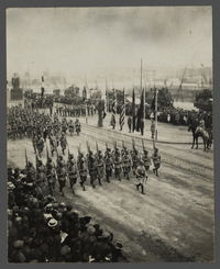Photographie d'un défilé militaire devant la foule, à l'arrière plan se trouvent les drapeaux des pays alliés