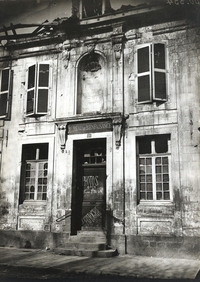 Photographie noir et blanc montrant une maison sur la porte de laquelle il est écrit "Photographe".